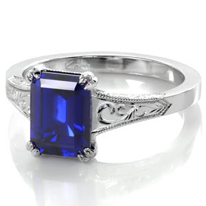 Sapphire engagement ring in Tulsa features a custom design with hand engraved patterns and hand wrought filigree curls. This antique engagement ring style inspiration is crowned with a stunning emerald cut blue sapphire.