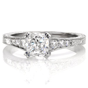Four pairs of double prongs exquisitely hold a 1.00 carat radiant cut center stone. Tapered diamonds along the band is met by an elegant scroll engraved pattern. The prongs showcase the side profile of the center diamond for a picturesque view. Full wheat engraving adorn the sides for an antique appeal. 