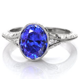 A flared, mil-grained knife-edge band gives Design 4002 an unmistakable vintage inspiration. The 2.00 carat lustrous oval-cut center blue sapphire is bezel set and framed by two diamonds on either side. The band is further detailed with hand formed filigree, micro pavé diamonds and hand engraving.