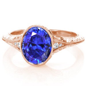 A flared, mil-grained knife-edge band gives Design 4002 an unmistakable vintage inspiration. The 2.00 carat lustrous oval-cut center blue sapphire is bezel set and framed by two diamonds on either side. The band is further detailed with hand formed filigree, micro pavé diamonds and hand engraving.