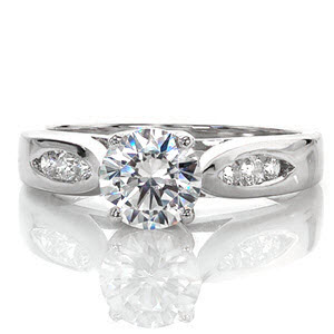 This contemporary ring is awe inspiring and uses minimal details to put all the focus on the 1.00 carat round brilliant cut center diamond. The elegantly swooping shoulders of the cathedral setting are made delicate by the open windows of the side profile. The top of the band has two pockets of channel set diamonds.