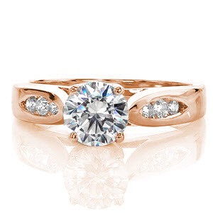 This contemporary ring is awe inspiring and uses minimal details to put all the focus on the 1.00 carat round brilliant cut center diamond. The elegantly swooping shoulders of the cathedral setting are made delicate by the open windows of the side profile. The top of the band has two pockets of channel set diamonds.