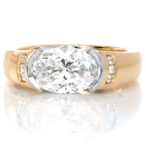 This custom ring is uniquely designed to hold a 1.50 carat oval cut diamond horizontally in a platinum half-bezel setting. The high polished 14K yellow gold band features vertical channel set diamonds. A stunning two-tone look is finished with perfectly placed platinum hand wrought filigree.