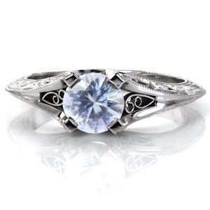 A light blue round cut sapphire adds to the vintage-inspired look of Design 3173.  Details surround the unique 4-prong set center stone including scroll hand engraving on the knife edge band, four pockets of hand-formed filigree curls and milgrain texture.