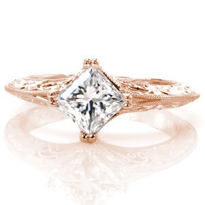 Design 3228 is a mesmerizing contrast of angles and curves. The crisp lines of the kite set princess cut center diamond are mirrored in the knife edged band style. The pockets of hand wrought filigree curls and the carefully hand carved, scroll pattern relief engraving add a graceful vintage appeal.