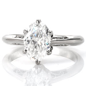 This stunning antique inspired engagement ring design features a 1.50 carat oval center stone in a six prong setting. The elegant band tapers at the top to seamlessly blend with the delicate petals adorning the base of the center stone. Graceful, hand crafted filigree curls give this piece vintage appeal.