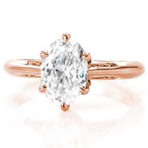 This stunning antique inspired engagement ring design features a 1.50 carat oval center stone in a six prong setting. The elegant band tapers at the top to seamlessly blend with the delicate petals adorning the base of the center stone. Graceful, hand crafted filigree curls give this piece vintage appeal.