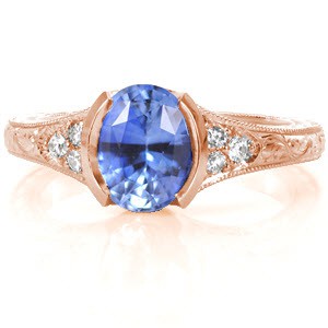 Des Moines custom rose gold engagement ring with an oval cut cornflower blue sapphire held in a half bezel setting with a hand engraved band.