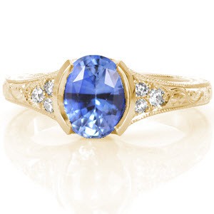 Providence custom engagement ring with an oval cut cornflower blue sapphire held in a half bezel setting with a hand engraved band.