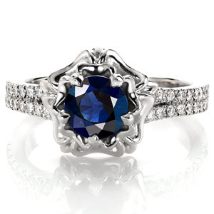 Design 3244 displays a rich 1.10 carat round cut blue sapphire in a distinctive double halo.  Crafted in 14 karat white gold, the micro pave band has a slight split shank as it reaches the halo. A double layer of high polished petals cup the sapphire and five prongs blend into the design seamlessly.
