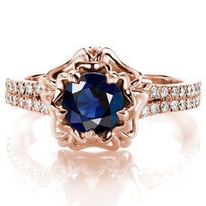 Design 3244 displays a rich 1.10 carat round cut blue sapphire in a distinctive double halo.  Crafted in 14 karat white gold, the micro pave band has a slight split shank as it reaches the halo. A double layer of high polished petals cup the sapphire and five prongs blend into the design seamlessly.