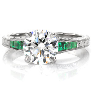 Design 3249 is a lavish juxtaposition of a 1.70 carat round brilliant center diamond against the rich green of its emerald side stones. The tapered band features vintage elements including three faces of hand engraving and hand wrought filigree curls. Its edges are given a refined finish with the addition of milgrain.