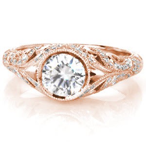 The Fitzgerald evokes images of the elegant 1920's and the decadent gems worn during that time. A bezel set center stone is the focus of a band made from swirling patterns. The upper scrolls are adorned with round brilliant diamonds while the lower sections are masterfully hand engraved with relief style scroll-work. 