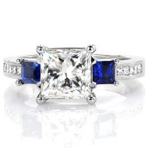 Design 3271 takes a modern look with graduating elevations and regal color accents. The center 1.50 carat princess cut diamond is flanked by two deep blue square cut blue sapphires. Continuing an elevation step, the band is dressed with channel set princess cut diamonds and woven trellis prongs.
