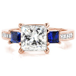Design 3271 takes a modern look with graduating elevations and regal color accents. The center 1.50 carat princess cut diamond is flanked by two deep blue square cut blue sapphires. Continuing an elevation step, the band is dressed with channel set princess cut diamonds and woven trellis prongs.