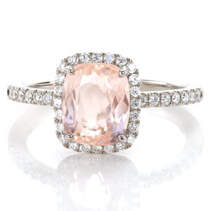 A 2.40 carat cushion cut morganite is delicately framed with a low-set halo of round cut diamonds. The high polished band of 14k white gold is ornamented with diamonds that are set within unique U-Cut hand formed prongs. Adding special detail, the basket is fully adorned with diamonds.
