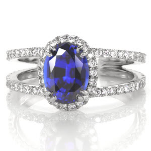 A grand 1.50 carat oval cut blue sapphire creates a beautiful statement of sophistication for our Maverick design. Crafted in 14k white gold, hand formed U-Cut prongs accentuate diamonds around the halo and band. A split shank flares towards the center stone and also tapers at the band bottom for a comfortable fit.