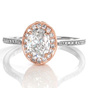 Design 3364 is a custom engagement ring modified from its original design into a two tone masterpiece. A 1.00 carat oval cut diamond is set into a rose gold central arrangement and surrounded by a flattering diamond halo. The contrasting white gold diamond band interlocks into this antique detailed setting.