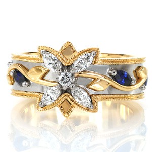 Design 3382 is an intricate composition of contrasting metals, floral motifs and sparkling gemstones. Rich yellow gold and elegant white gold act as a base for the flowing vines, spotted with marquise blue sapphires, leading up the sides of the band. Round and marquise diamonds create the central flower design.