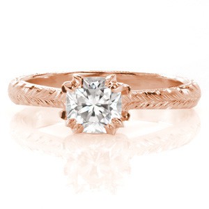 A luminous 0.70 carat cushion cut center diamond is the star of this custom engagement ring. Design 3392 offers a wheat style hand engraved and milgrain edged band tapering towards the square ratio center stone. A surprising marquise diamond floral design decorates the profile view.