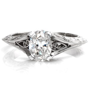 Design 3394 is a vintage inspired solitaire engagement ring build around a dazzling 0.70 carat oval cut center diamond. The knife edge band flares allowing room for pockets of hand formed filigree curls to nestle against the center stone. Additional filigree, relief engraving and milgrain edging decorates the profile. 