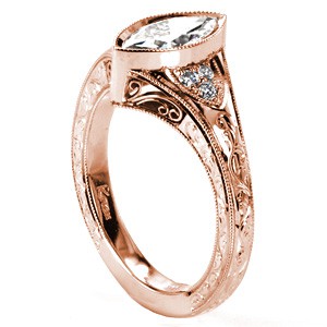 Unique rose gold engagement rings in Seattle feature hand engraved pattern and elegant hand formed filigree curls. The bezel set center diamond is shown as a marquise diamond.