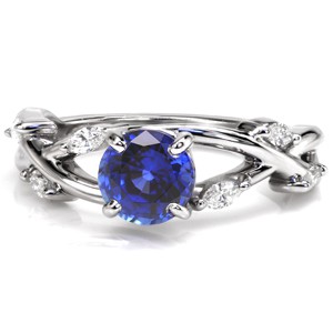 A stunning deep blue round-cut sapphire is the chromatic focus within our custom ring Design 3436. Framing the center stone is a twisting vine-like band studded with leaf-shaped marquise diamonds. A four-prong basket setting is incorporated into the flowing lines of the ring.