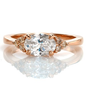 Champagne side diamonds in 14 karat yellow gold create an elegant frame for the 1.00 carat oval center diamond. The horizontal setting flows seamlessly into the clusters of side diamonds and then the tapered band. Putting all the focus on the top of the design allows for a low profile setting.