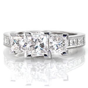 Design 3463 is a contemporary three stone custom engagement ring with subtle vintage inspired details. Three princess cut diamonds take center stage, set into four prong chevron settings. Milgrain edging borders the channel set princess cut side diamonds, and a floral design can be seen on the ring's profile.