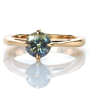 A gorgeous mosaic-like blue-green round sapphire draws the spotlight in this unique custom ring setting. Design 3471 reinterprets a classic engagement ring outline with the addition of an exaggerated profile cathedral and a rotated four prong center setting. 