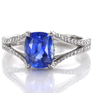 A breathtaking statement, Design 2472 places focus on the 2.00 carat cushion cut blue sapphire center gemstone.  The decorated split shank band is detailed with individually hand-set  micro pavé. Diamonds also decorate the basket, adding more sparkle to the profile view. 