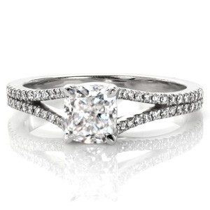 The graceful split shank of the Cushion Bianca creates the perfect contemporary balance of simplicity and style. Set with a 1.00 carat cushion cut center diamond, this four prong setting creates an intricate trellis woven detail. The diamond band gently flares into two rows of diamonds as it reaches the center stone.