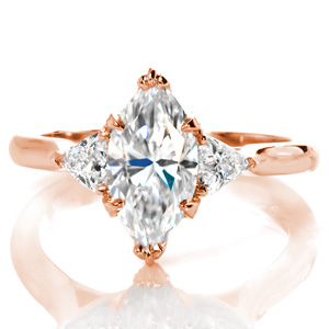 This stunning three-stone design is shown with a unique combination of diamond shapes. The points of the trillion sides are a perfect complement to the marquise center. The crown of each stone is detailed with beadset round brilliant diamonds with hand applied milgrain borders. 