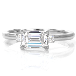 Elegant simplicity creates a gorgeous three stone design with an East-West set emerald cut center diamond and small, asscher cut side stones. The mesmerizing mirrored facets of these step-cut stones are complimented by the smooth, high polished luster of the metal.