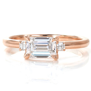 Elegant simplicity creates a gorgeous three stone design with an East-West set emerald cut center diamond and small, asscher cut side stones. The mesmerizing mirrored facets of these step-cut stones are complimented by the smooth, high polished luster of the metal.