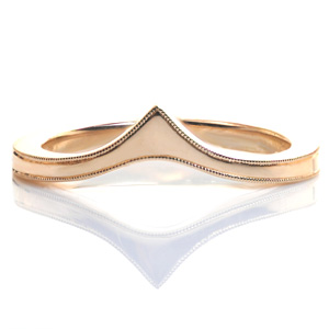 An elegant band, Design 3557 is uniquely shaped to be worn as a contoured wedding band against an engagement ring, alone, or as part of a stacking set. The band tapers as it reaches the top before flaring out again into a point. The top edges of the piece are delicately hand detailed with a beaded milgrain texture.