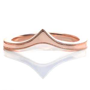 An elegant band, Design 3557 is uniquely shaped to be worn as a contoured wedding band against an engagement ring, alone, or as part of a stacking set. The band tapers as it reaches the top before flaring out again into a point. The top edges of the piece are delicately hand detailed with a beaded milgrain texture.