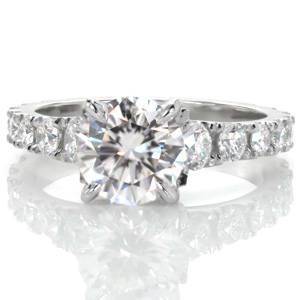 A magnificent diamond engagement ring shown with a 1.50 carat round brilliant center stone, Design 3561 is simply regal. The flared band is hand crafted with U-Cut pavé settings to the graduating diamond side stones. The sides of the setting are elegantly detailed with diamond-set petals.