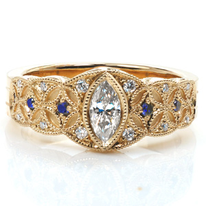 Design 3563 is an antique inspired low profile design with a gorgeous star-burst pattern. A bezel set marquise center stone crowns the flared band while milgrain on the edges highlight the design. Small diamonds and blue sapphires add light and sparkle the band. The sides are hand engraved with a half-wheat pattern.