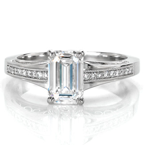 Design 3567 is an elegant antique inspired piece shown with an emerald cut center diamond. The flared band compliments the elongated shape of the step cut stone, while milgrain edged rows of round brilliant diamonds add sparkle to the top of the band. The sides are detailed with graceful, flowing hand wrought filigree.