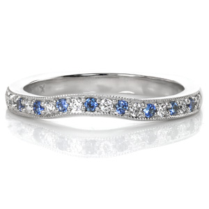 Pale, light blue sapphires add a delicate touch of color do this contoured wedding band design. A custom design, this band has been crafted with a squared Euro shank base. The gentle contour of the top is always custom drawn to fit the ring it will sit with. Beaded milgrain texture adds a vintage touch to the edges.
