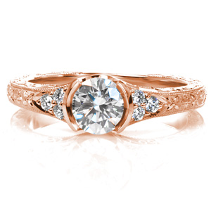 This organically inspired engagement ring features a low, half-bezel setting with a flared band. The spectacular relief engraving on the top and sides of the piece takes form as delicate flowers and flowing, curling vines. Hand wrought filigree curls fill the pockets to either side of the center stone.