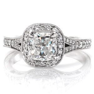 Classic antique details are brought to life in exquisite beauty with this split-shank halo engagement ring. The center is shown as a cushion cut diamond surrounded by a micro pavé double sided halo. The band is additionally adorned with delicate hand engraving, hand wrought filigree curls, and milgrain detail. 