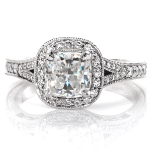 Classic antique details are brought to life in exquisite beauty with this split-shank halo engagement ring. The center is shown as a cushion cut diamond surrounded by a micro pavé double sided halo. The band is additionally adorned with delicate hand engraving, hand wrought filigree curls, and milgrain detail. 