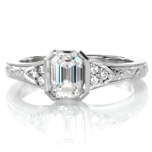 Design 3577 is a beautiful flared design featuring an emerald cut center diamond held in a half-bezel setting. The top of the antique inspired band is adorned with hand engraved scroll patterns and edged with a beaded milgrain texture. Clusters of round brilliant diamonds frame the center stone.