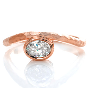 The gentle curves of the band are designed to gracefully hold the East-West bezel set center diamond. A hammered texture is hand applied to the top of the band and then given a sand-blasted finish. The bezel and sides of the band shine with a high polished luster in contrast to the top of the band for added appeal.