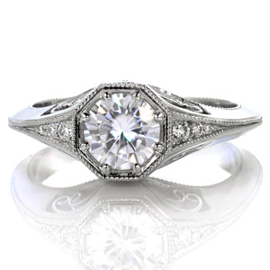 Elegantly crafted, this ring features a knife-edge band with an octagonal center setting. The flared band perfectly flows into the under-bezel basket allowing for small bead-set diamonds on the top. Open pockets in the basket feature delicate hand wrought filigree curls. Milgrain adds texture to the edges of the piece.