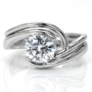 This flowing band is a perfect match to our Ripple design with its sleek lines and gentle curves. The band is kept at all one height to create a variation of elevations for extra focus on the center diamond. The smooth luster of the high polished metal helps to accentuate the beautiful wrap of the center setting.