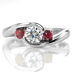 Lush red rubies flank a round brilliant center diamond in this contemporary design. The center stone is wrapped in a half-bezel setting with a tapering band. The smooth, high polished metal of the band adds a shiny luster to the design to compliment the sparkle from the gem stones. 