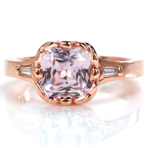 Design 3608 features a unique pale pink cushion cut center sapphire in a custom floral bezel setting style. This beautiful design features antique inspirations. Tapered baguette diamonds on the flared band add an extra hint of sparkle, while hand wrought filigree curls add detail to the basket of the setting. 